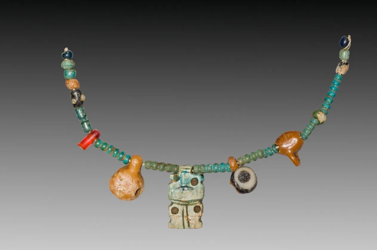 Fragment d'un collier ancien : une rangée de perles et de pendentifs en pierre aux tons chauds, délicat travail féminin