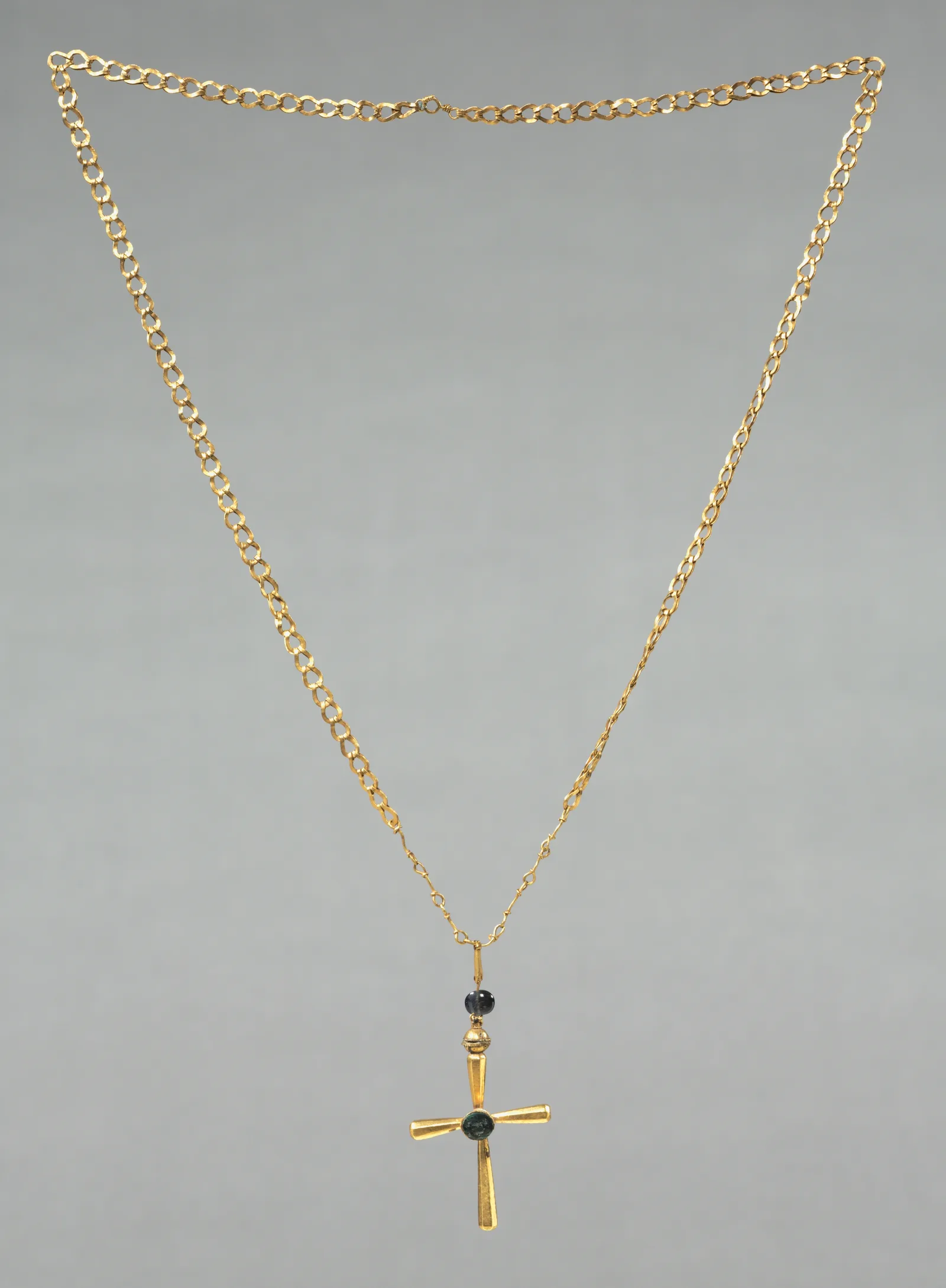 Cadena de eslabones de oro con una cruz latina colgante de brazos ensanchados y una piedra oscura en el cruce y una cuenta azul encima, Bizancio, siglo VI